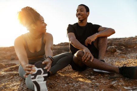 Cheerful millennial african american lady, man in sportswear stretching legs, relax after trainingの写真素材
