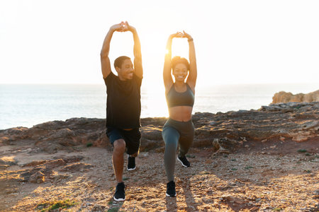 Glad young african american female and man in sportswear doing stretching, practice yogaの写真素材
