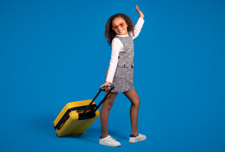 Happy teen african american curly girl tourist in sunglasses with suitcase enjoy travelの写真素材
