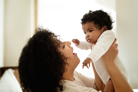 Cheerful young african american curly woman playing with little child, enjoy relax and tender moment togetherの写真素材