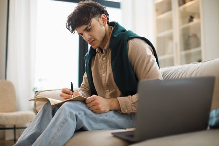Man Taking Notes Near Laptop Having Issues Learning At Homeの写真素材