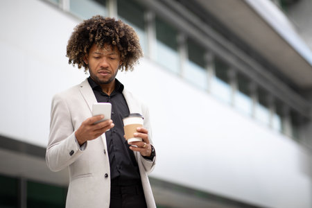 African american middle aged male entrepreneur holding takeaway coffee and using cellphone while walking outdoorsの写真素材