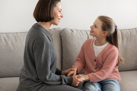 Positive european millennial mother holding hand, talk with teenage girl, enjoy communication in living roomの写真素材