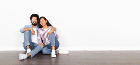 Happy indian couple sitting on floor against white wallの写真素材