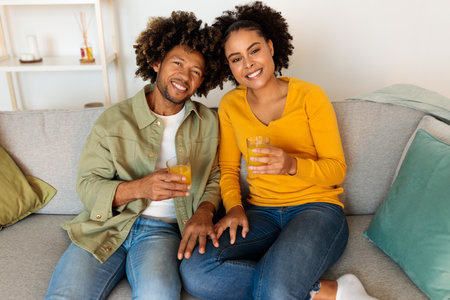 Cheerful African Couple Drinking Orange Juice Holding Glasses At Homeの写真素材