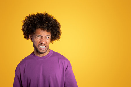 Angry sad adult african american curly man in purple t-shirt looking at empty spaceの写真素材