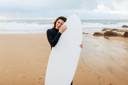 Happy young lady posing with surfing board, smiling at camera, enjoying holiday and water sports, standing on beachの写真素材