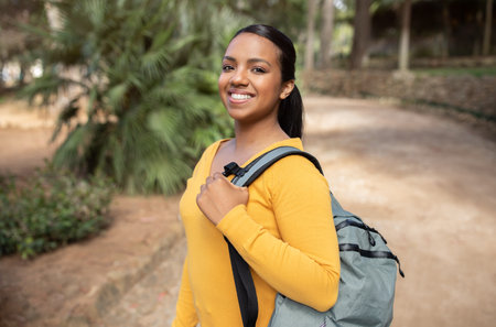 Glad happy brazilian student lady in casual with backpack looking at camera and smiling, walking in park, free spaceの写真素材