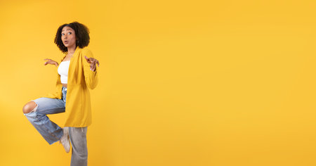 Having fun. Happy young black lady jumping, dancing and looking aside at copy space, yellow background, panoramaの写真素材