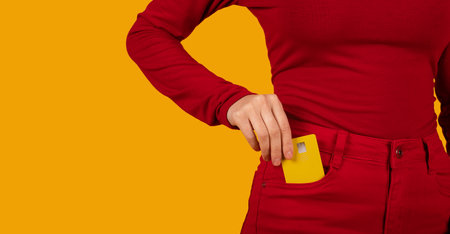 Woman putting yellow bank card in red pants pocket, croppedの写真素材