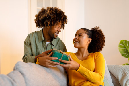 Cheerful Black Husband Giving Gift Box Congratulating Wife At Homeの写真素材