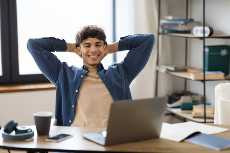 Happy Young Man Looking At Laptop Relaxing At Workplace Indoorsの写真素材
