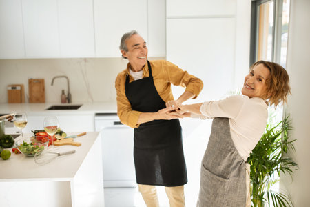 Romantic senior couple dancing, having fun together at music in kitchen interior, copy spaceの写真素材