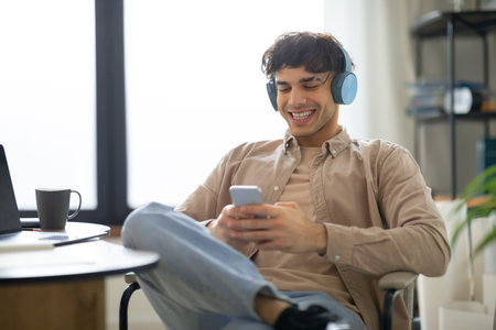 Cheerful Man Using Cellphone Wearing Headphones Listening Music At Homeの写真素材