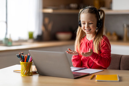 Cute little schoolgirl having video call with tutor, talking to laptop webcameraの写真素材