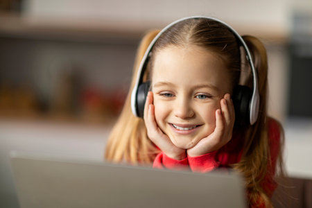 Smiling Little Girl Wearing Wireless Headphones Using Laptop At Home