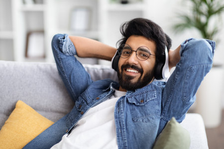 Handsome Young Indian Guy Wearing Wireless Headphones Listening Music At Homeの写真素材