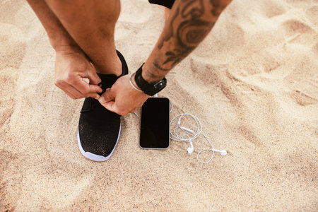 Runner man tying running shoes laces getting ready for run with smartphone and earphones near him, mockup, copy spaceの写真素材