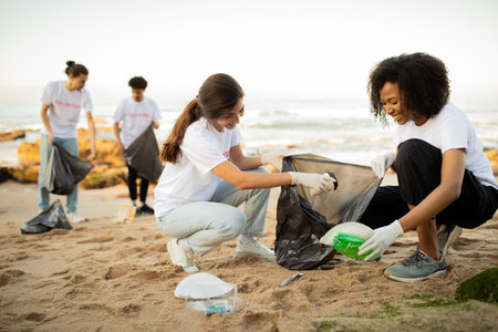 Positive young different people volunteers in gloves with garbage bags clean up trash on sea beachの写真素材
