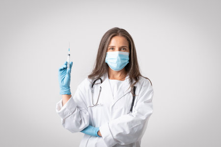 Immunization concept. Senior doctor woman in medical mask holding syringe with vaccine dose ready to make injection shotの写真素材