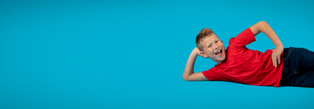 Cheerful Male Child Relaxing On Floor While Posing Isolated On Blue Backgroundの写真素材