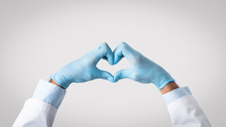 Hands of old european doctor in white coat and protective gloves makes heart gestureの写真素材