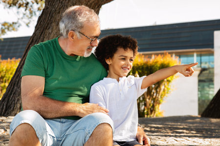 Smiling little mixed race boy pointing finger at empty space to european grandfather, enjoy free timeの写真素材