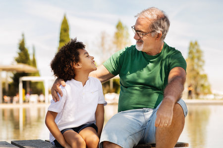 Positive mature caucasian grandfather and little mixed race boy enjoy free time, communicate, have...