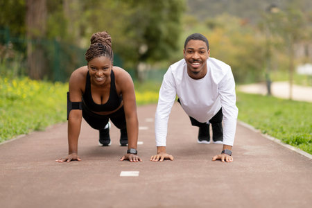 Cheerful young african american couple doing push up exercise in park outdoor, enjoy training at summerの写真素材
