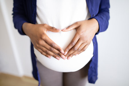 Millennial african american pregnant lady with big belly making heart sign with hands in living roomの写真素材