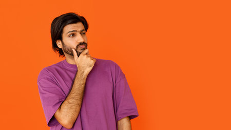 Curious hindu guy looking at copy space, touching faceの写真素材