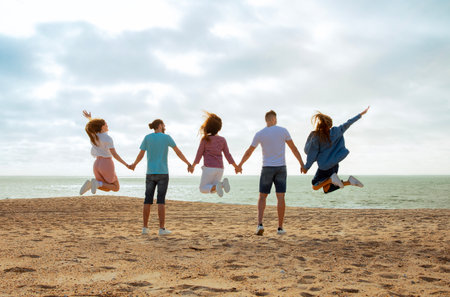Happy millennial european and arab friends have fun, enjoy free time, jump, freeze in air on ocean...