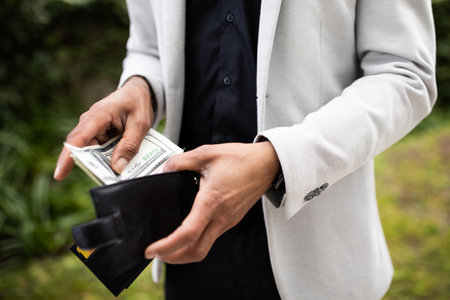 Unrecognizable black man taking out dollar cash money from wallet outdoors, pulling usd money...