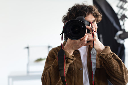 Male photographer taking photo with professional camera in photostudio, young man working on photo shoot, free spaceの写真素材