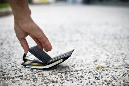 Closeup view of black man picking up lost wallet full of money banknotes on city street, selective focus, empty spaceの写真素材