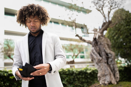 Im broke. Sad black middle aged male entrepreneur bankrupt looking in his empty wallet, standing outdoors, free spaceの写真素材