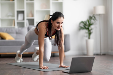 Beautiful athletic young woman have workout at home, using laptopの写真素材