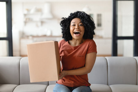 Happy Excited Black Woman Holding Cardboard Box With Delivery At Homeの写真素材
