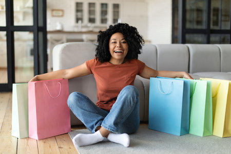Happy Young Black Woman Sitting On Floor Among Bright Shopping Bagsの写真素材