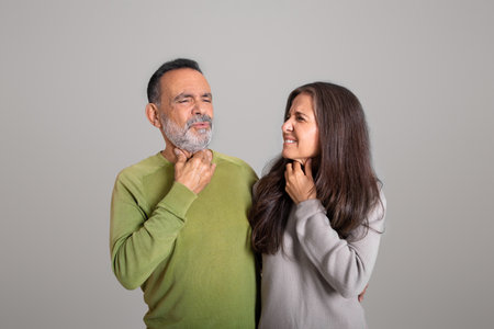 Sad european old couple suffer from sore throat, tonsillitis on gray studio background