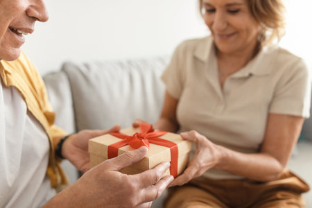 Cropped of senior wife and husband exchanging presents on anniversary day at home, spouses holding gift boxの写真素材