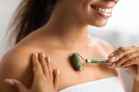 Smiling Black Woman Using Greenstone Jade Roller For Skin Care At Homeの写真素材