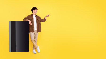 Guy Leaning On Large Credit Card Near Copyspace, Yellow Backgroundの写真素材