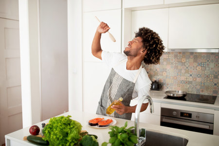 Black Cook Man Singing With Spoon In Hand In Kitchenの写真素材