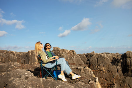 Happy Young Couple Relaxing In Camping Chairs On Rocky Coastの写真素材