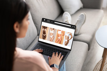 Millennial arabic woman shopaholic enjoy online shopping, buy underwear on laptop screen, sitting on sofaの写真素材