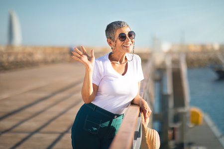 Smiling Mature Woman Waving Hand Posing At Pier With Sailboats