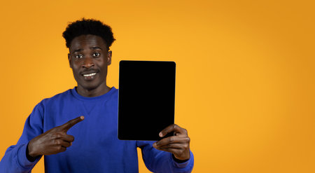 Cheerful black guy pointing at digital tablet with blank screenの写真素材