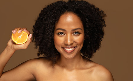 Cheerful half-naked young black woman holding half of orangeの写真素材