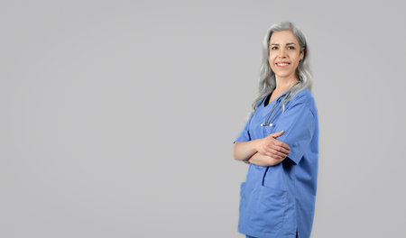 Smiling woman doctor in blue uniform posing on gray backgroundの写真素材